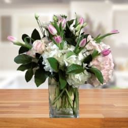 Pink tulips and pale hydrangeas in a clear glass vase