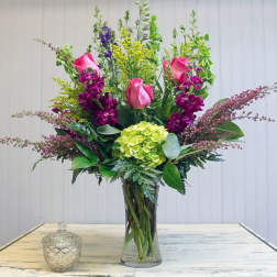 Tall bouquet of pink roses, purple blooms, and green hydrangea in a glass vase