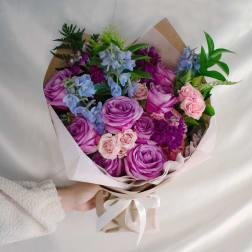 Bouquet of purple and pink roses with blue flowers wrapped in paper