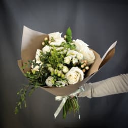 Bouquet of white roses and small white blooms wrapped in brown paper