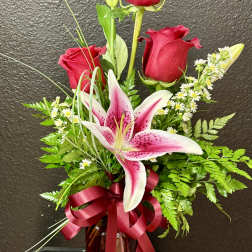 Tall arrangement of red roses and a pink stargazer-style lily in a red glass vase with ribbon