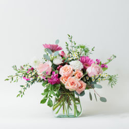 Pink and peach roses in a clear glass vase with mixed blooms