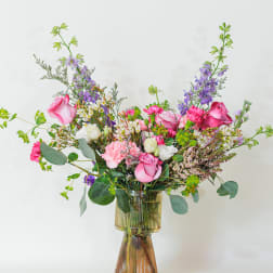 Tall mixed arrangement of pink roses, carnations, and purple flowers in a ribbed glass vase