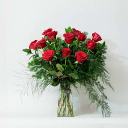 Red roses arranged in a clear glass vase with airy greenery