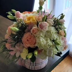 Mixed bouquet of pastel roses and hydrangeas in a plaid round box