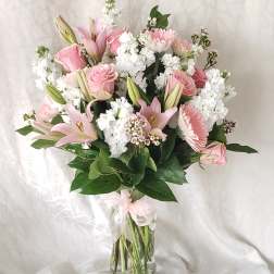 Pink lilies and roses arranged in a clear glass vase with white filler flowers.