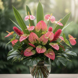 Pink anthuriums arranged in a clear glass vase with tropical leaves