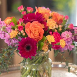 Mixed bouquet of orange, pink, and purple flowers in a glass jar vase