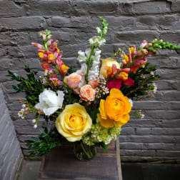 Mixed bouquet of roses, ranunculus, and snapdragons in a glass vase
