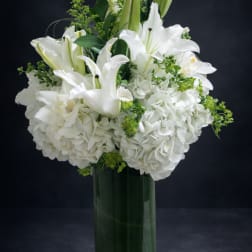 White lilies and hydrangeas arranged in a clear glass vase