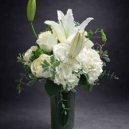 White lilies and roses arranged in a tall glass vase