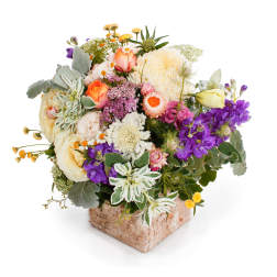 Mixed bouquet in a square bark-covered vase with cream, purple, and peach flowers
