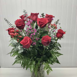 Tall arrangement of red roses with small pink blooms in a clear glass vase