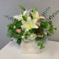 White lilies and pale pink roses arranged in a square vase