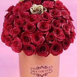 Red roses arranged in a gold round box with one gold rose
