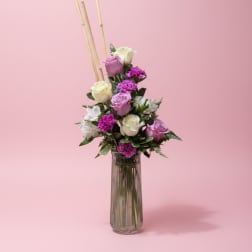 Pink and white roses with purple flowers in a tall glass vase