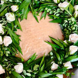 Wreath of white roses and greenery arranged in a circle on a flat base
