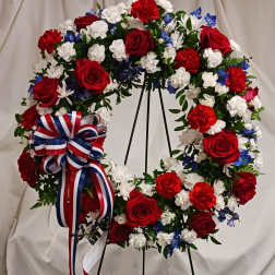 Circular wreath of red, white, and blue flowers on a stand with a ribbon bow