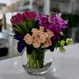 Bouquet of peach roses, purple tulips, and magenta orchids in a glass vase