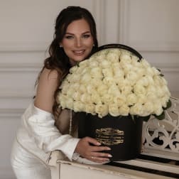 Large black hatbox filled with cream roses beside a smiling woman in white.