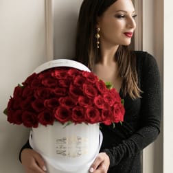 Woman in a black dress holding a round white box filled with dozens of red roses.
