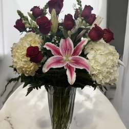 Bouquet of red roses, white hydrangeas, and a pink lily in a glass vase