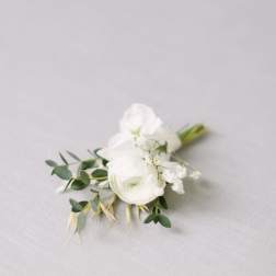 Small white floral boutonniere with greenery on a light fabric background