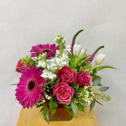 Pink gerberas and roses arranged in a low vase with white tulips.