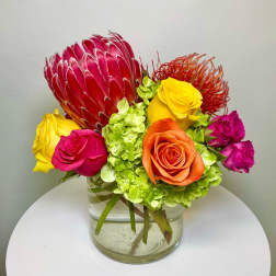 Colorful bouquet with roses, hydrangea, and a protea in a glass vase