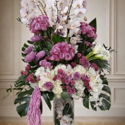 Tall floral arrangement with pink roses, white orchids, and hydrangeas in a glass vase