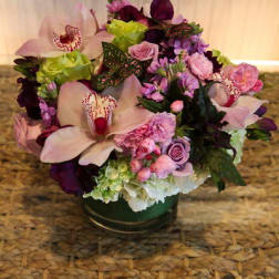 Low arrangement of pink orchids, roses, carnations, and hydrangeas in a clear glass vase