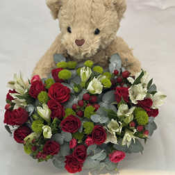Teddy bear holding a bouquet of red roses and white flowers
