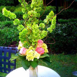 Tall floral arrangement with green orchids and pink roses in a glass vase