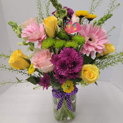 Mixed bouquet of pink, yellow, and purple flowers in a glass vase with a ribbon