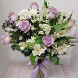 Lavender roses and white lilies in a glass vase with a purple ribbon