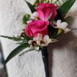 Pink rose boutonniere with white accent flowers and dark ribbon