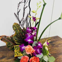 Tropical floral arrangement with purple orchids and coral roses
