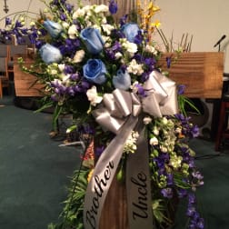 Large blue and purple floral spray on a wooden cross with a ribbon