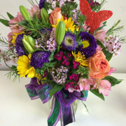 Colorful mixed bouquet in a clear glass vase with a red butterfly pick