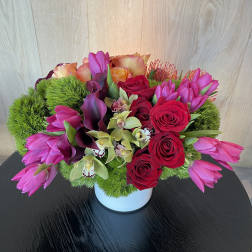 Pink tulips, red roses, and orchids arranged in a white vase
