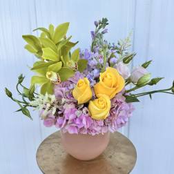 Bouquet of yellow roses, green orchids, and pink hydrangeas in a blush vase