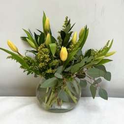 Yellow tulip arrangement with foliage in a round clear glass vase