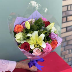 Bouquet of multicolored roses and white lilies wrapped in purple paper