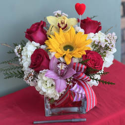 Bouquet of red roses, a yellow sunflower, and pink orchids in a glass vase