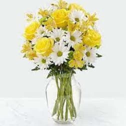Yellow roses and white daisies in a clear glass vase