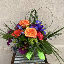 Colorful bouquet with orange roses, purple irises, and a green ribbon in a vase