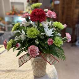 Small bouquet of red, white, and green flowers in a textured vase with a ribbon