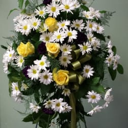 Tall standing floral spray with white daisies and yellow roses on a ribboned easel