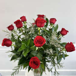 Arrangement of long-stem red roses with small white filler flowers in a clear glass vase