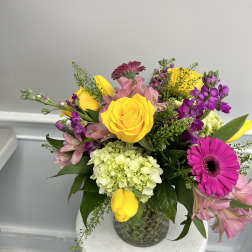 Mixed arrangement of yellow roses and tulips with pink and purple blooms in a clear glass vase